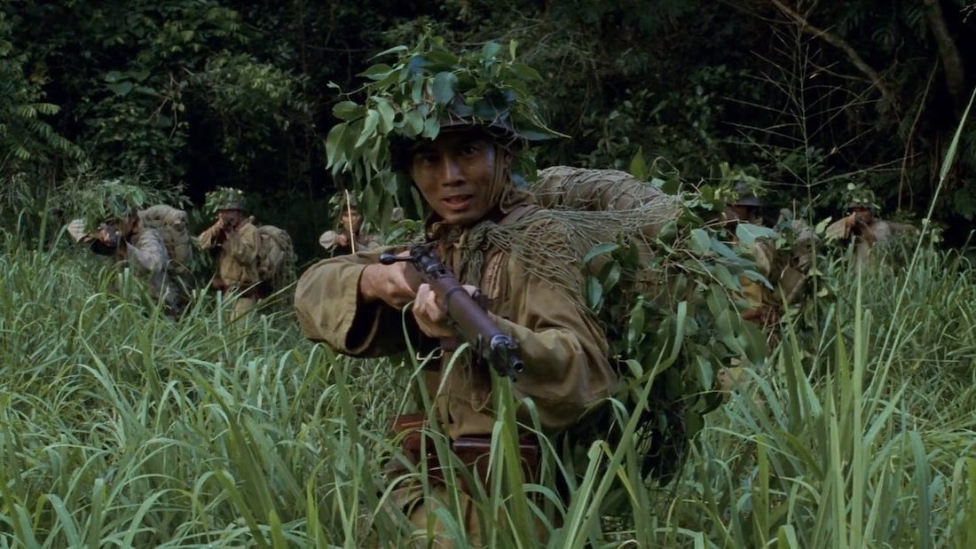 Japanese soldiers stare at someone or something beyond the camera, the jungle behind them.